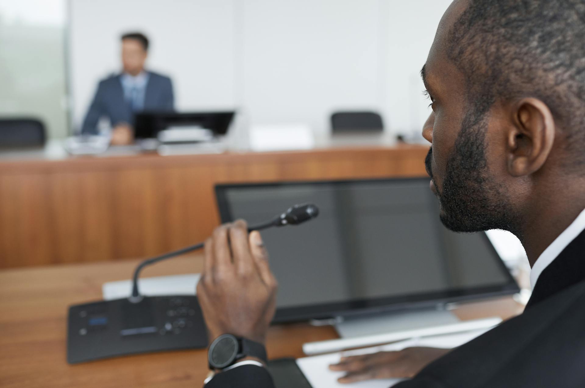 Bearded businessman speaks into microphone during office conference.