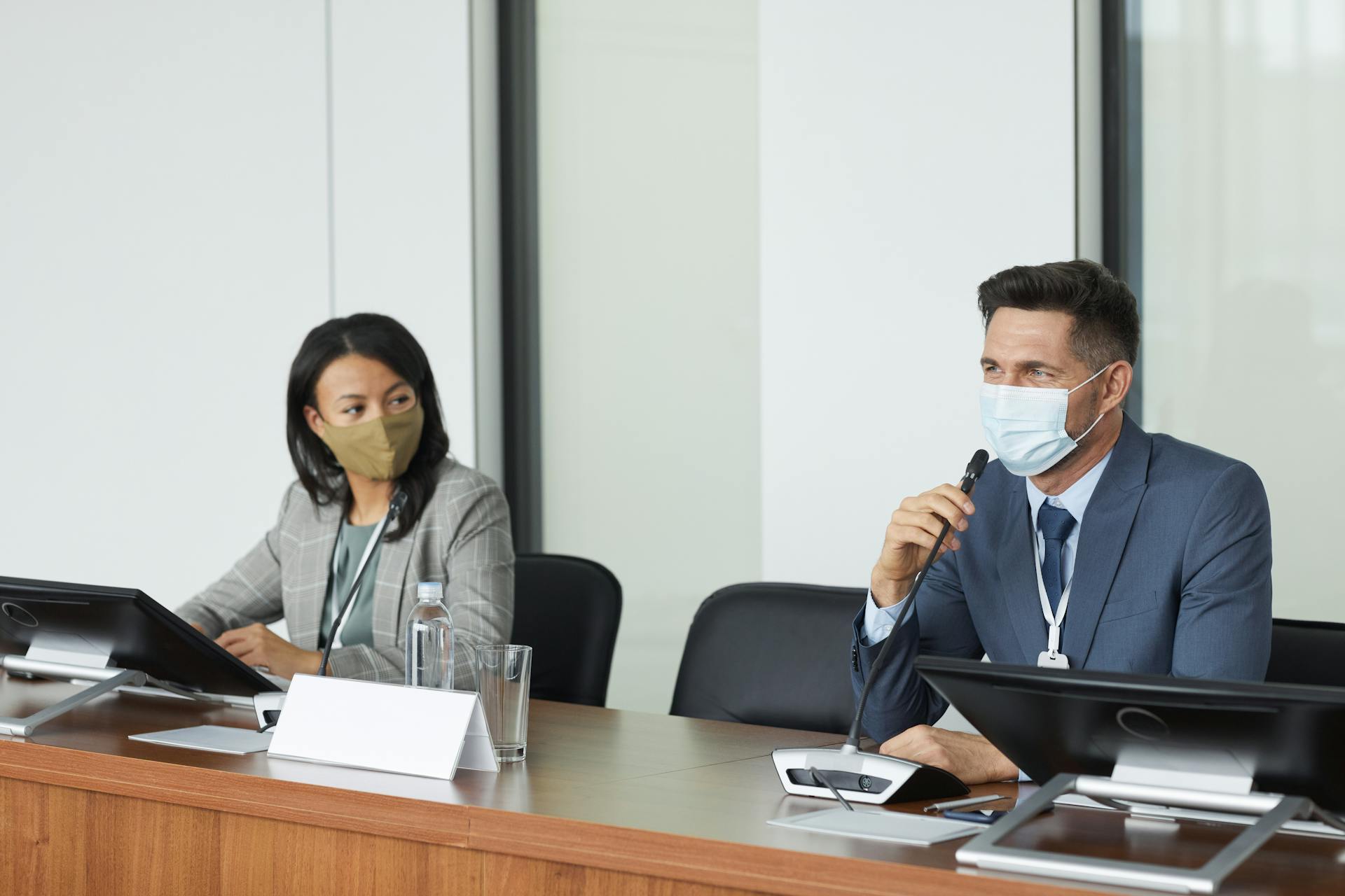 Two masked professionals in a conference room discussing business matters.