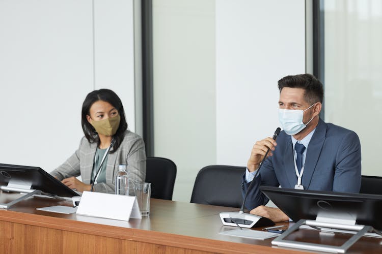 A Man In Blue Suit Wearing A Face Mask While Having A Conference Meeting