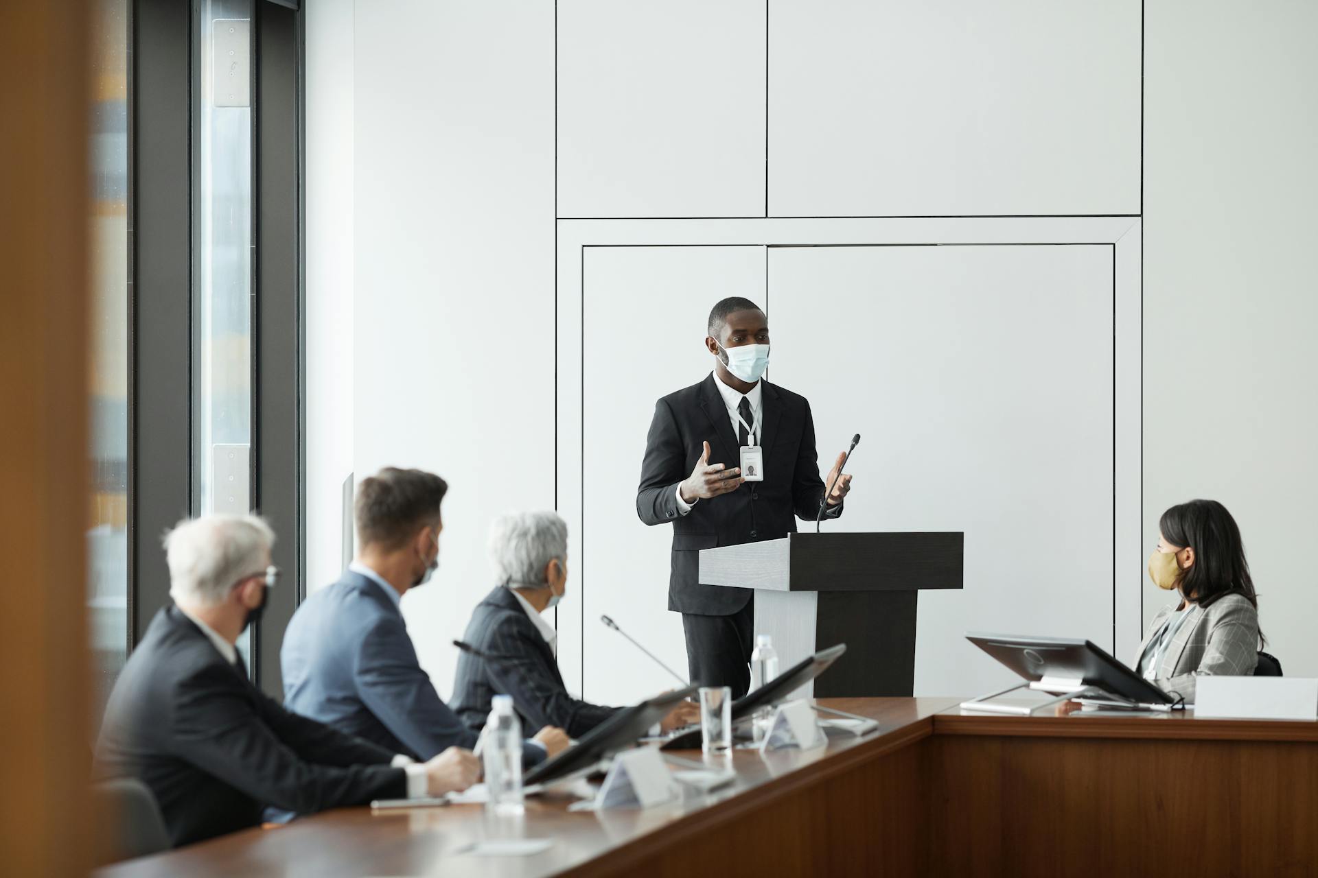 Business professionals in masks hold a meeting indoors, highlighting new normal practices during pandemic times.