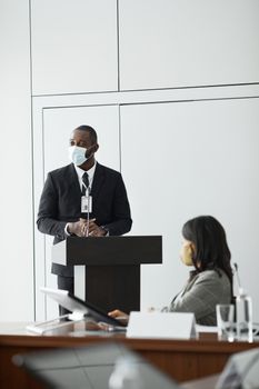 A professional conference featuring masked speakers and attendees maintaining safety protocols indoors.
