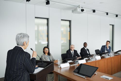 Elderly Woman Speaking In Front of People in a Conference Room 