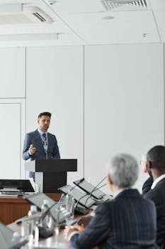 A man in a blue suit giving a presentation at a conference podium indoors.