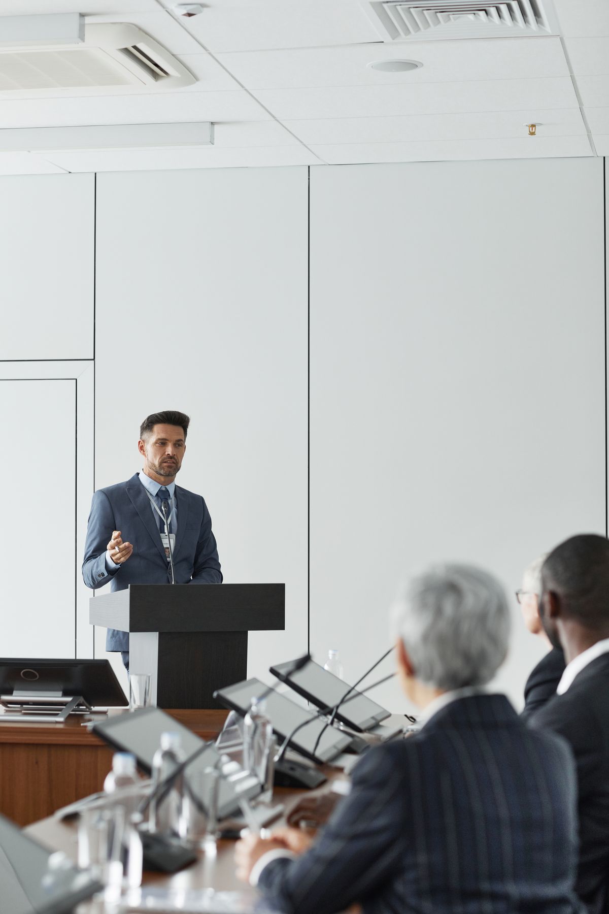 A presenter at a podium delivering a deck to a small conference-room audience