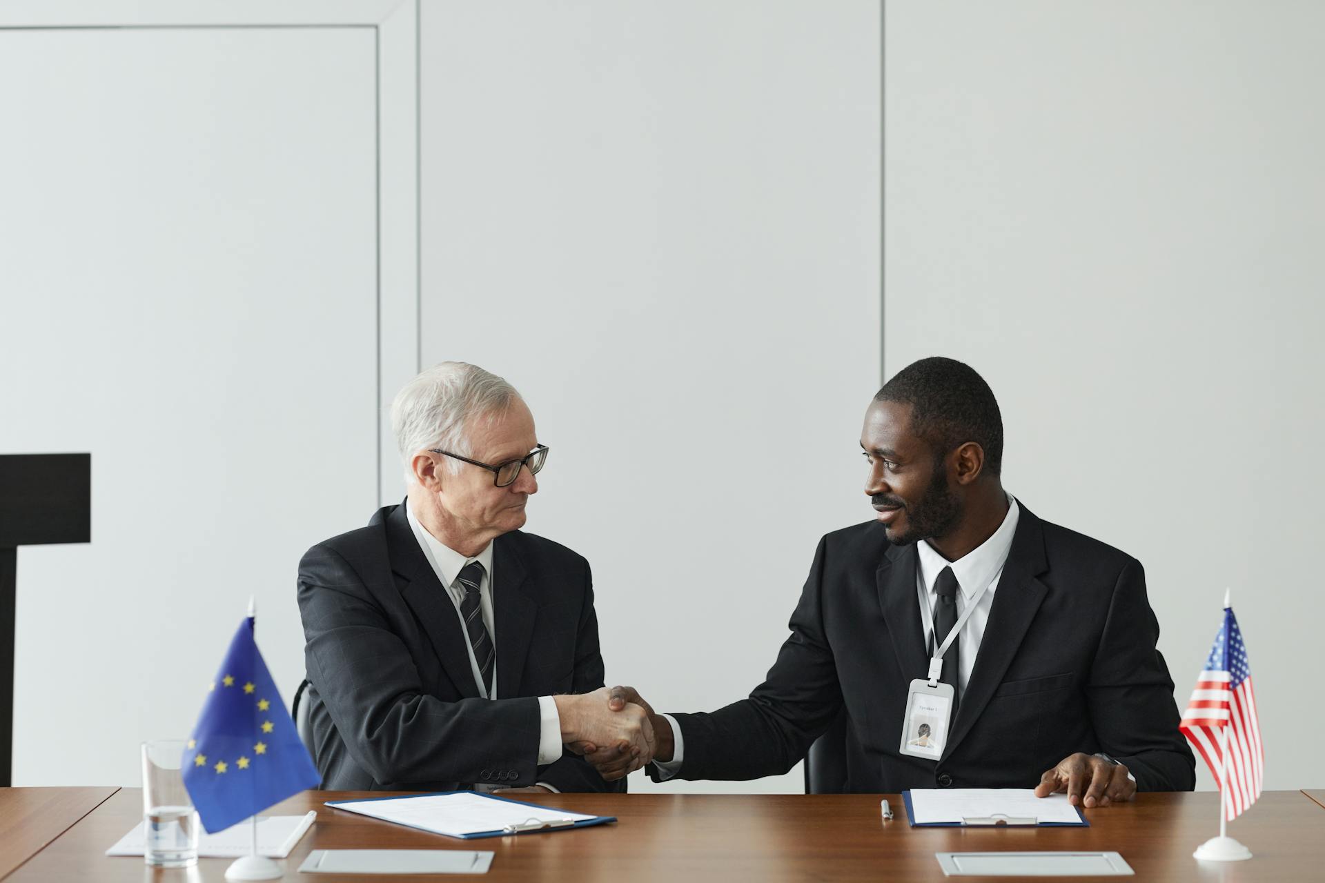 Corporate handshake between diverse businessmen representing EU and US flags, symbolizing partnership and collaboration.