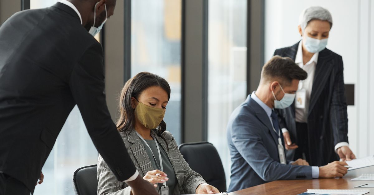 Business professionals wearing face masks in a meeting room, maintaining safety protocols.