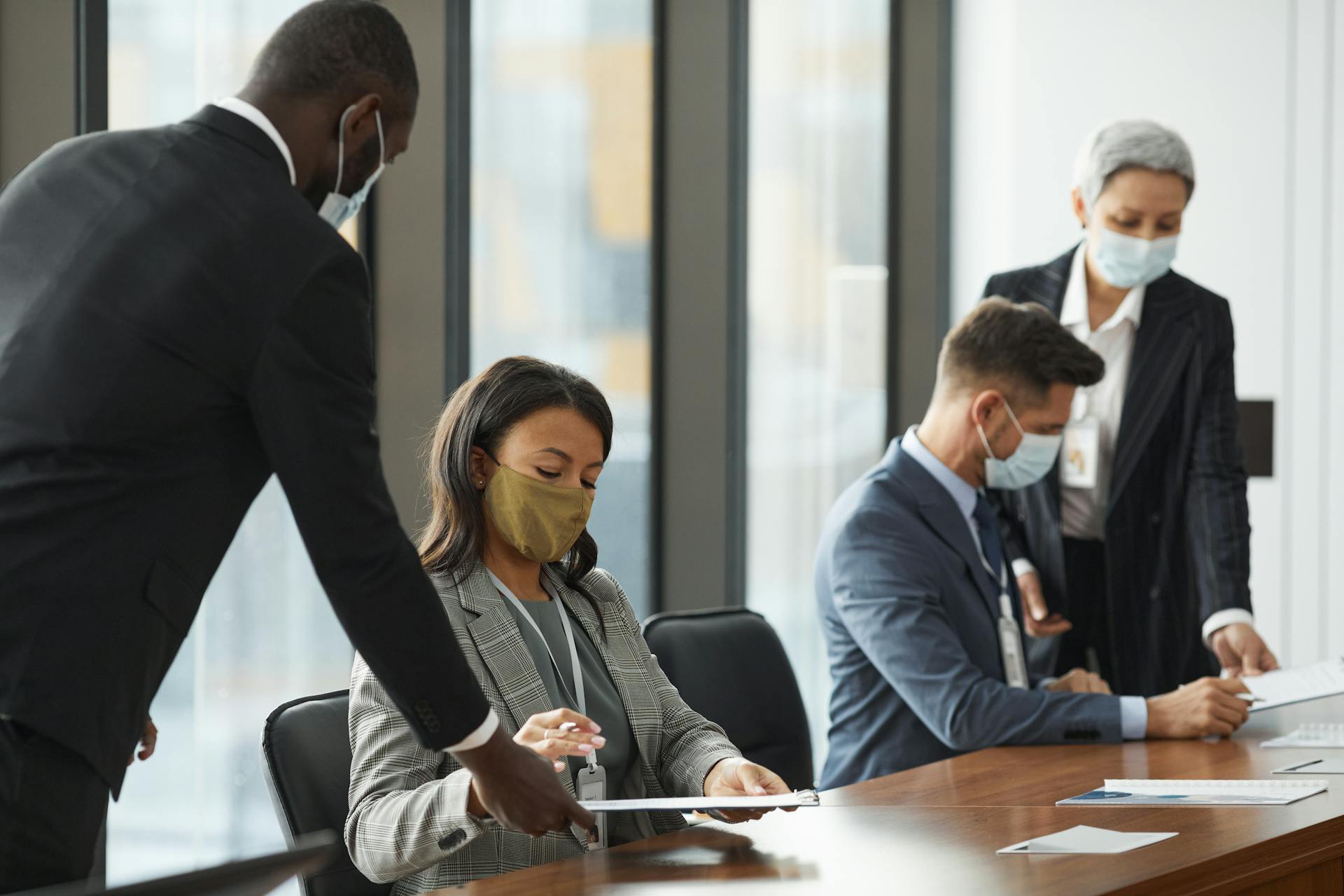 Business professionals wearing face masks in a meeting room, maintaining safety protocols.