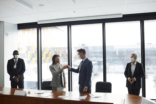 Diverse professionals in formal attire fist bumping at a business meeting in a conference room.