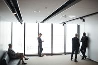 Man in Black Suit Standing Near Glass Window