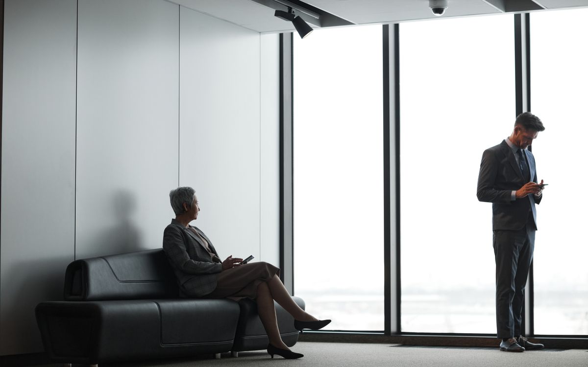 Business professionals in formal attire waiting in a modern office lobby.
