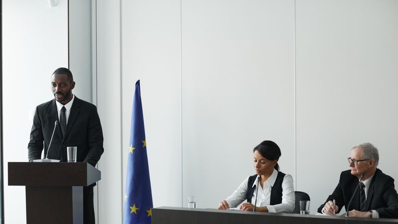 Professional business conference with EU flag, diverse speakers in suits discussing diplomacy.
