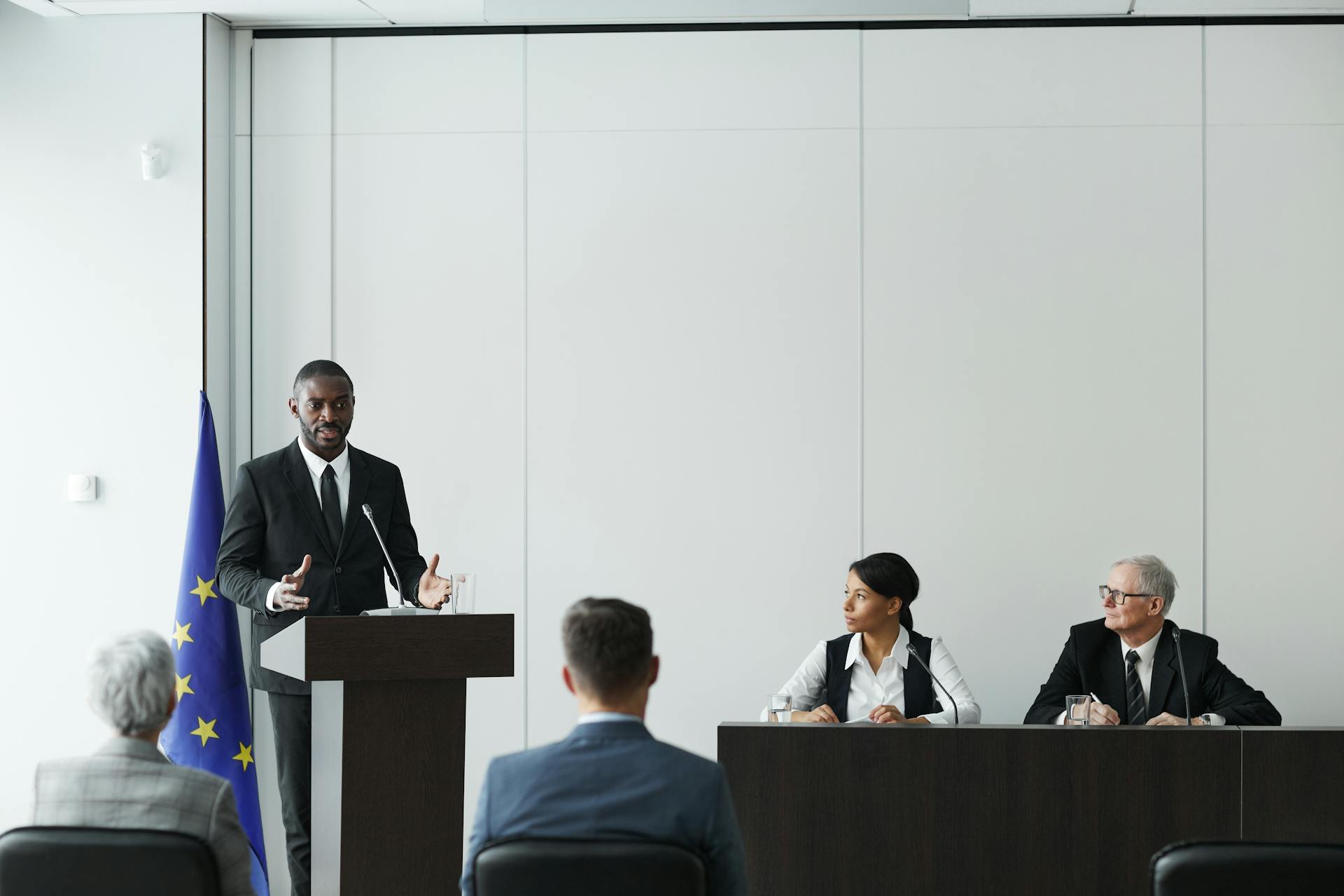 Business meeting featuring diverse professionals discussing important topics with a speaker at the podium indoors.