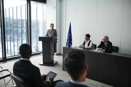 Free Professional conference setting with a speaker at a podium and attentive audience in a modern meeting room. Stock Photo