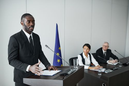 Free Business professional delivering speech in conference with colleagues listening attentively. Stock Photo