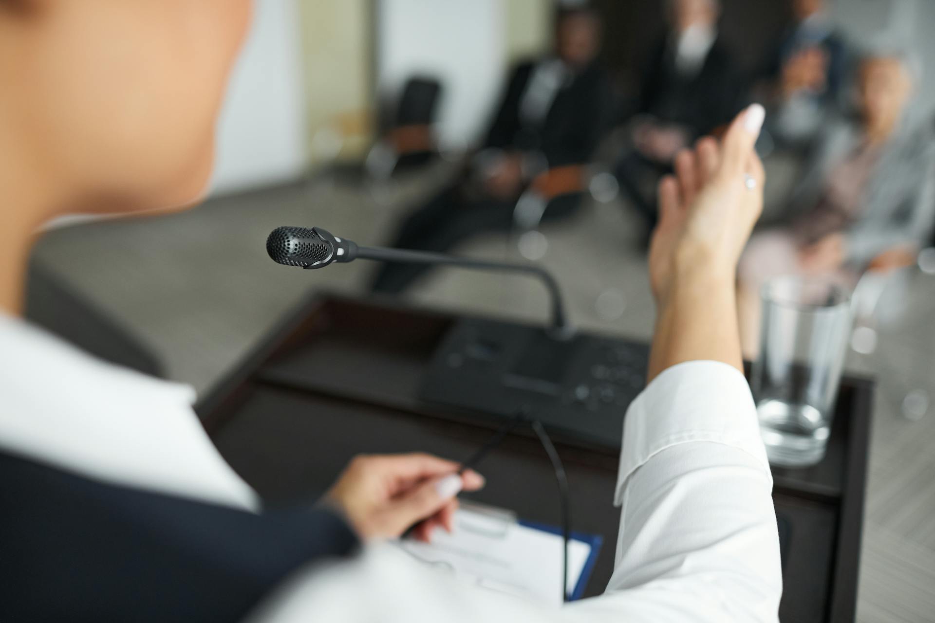 A person speaking at a podium with a microphone to an audience during a business meeting.