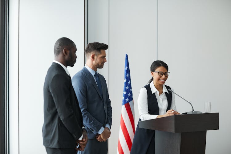 Men In Business Attire Looking At The Woman Talking Near The Podium