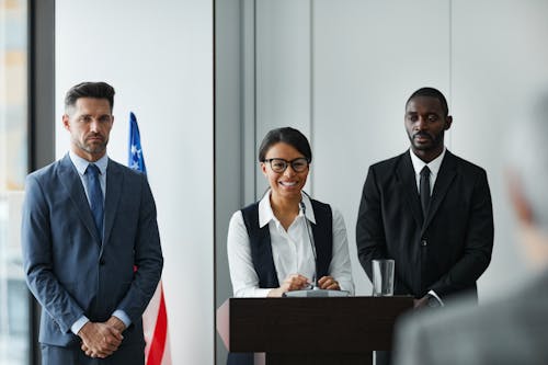 Woman Standing at a Rostrum with Two Men in Suits next to Her during a Political Conference 