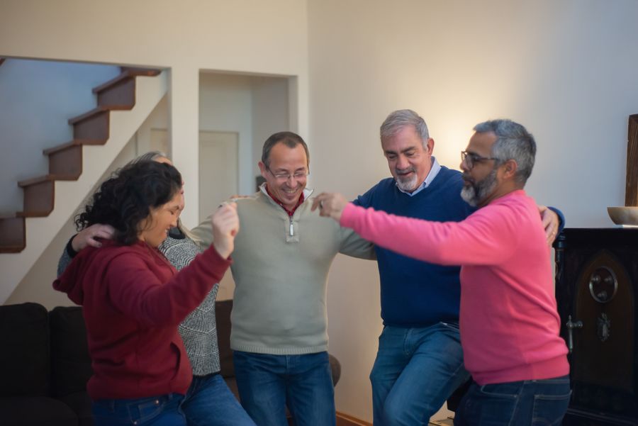 An adult with Down syndrome and three team members join hands together outdoors, all smiling.