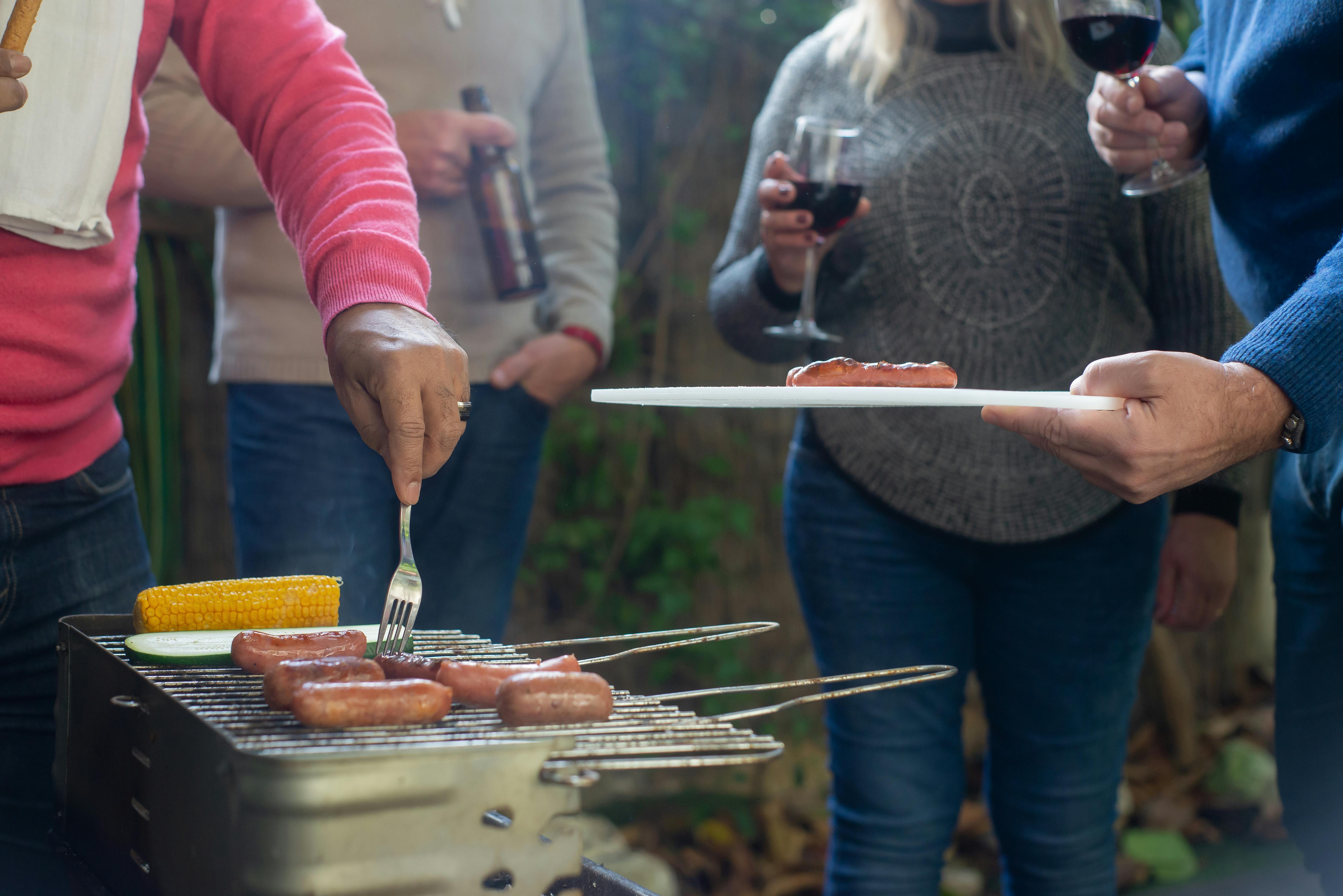 Friends enjoying a barbecue with sausages and red wine outdoors.