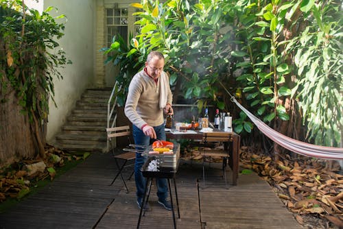 An Elderly Man Grilling Food at the Backyard