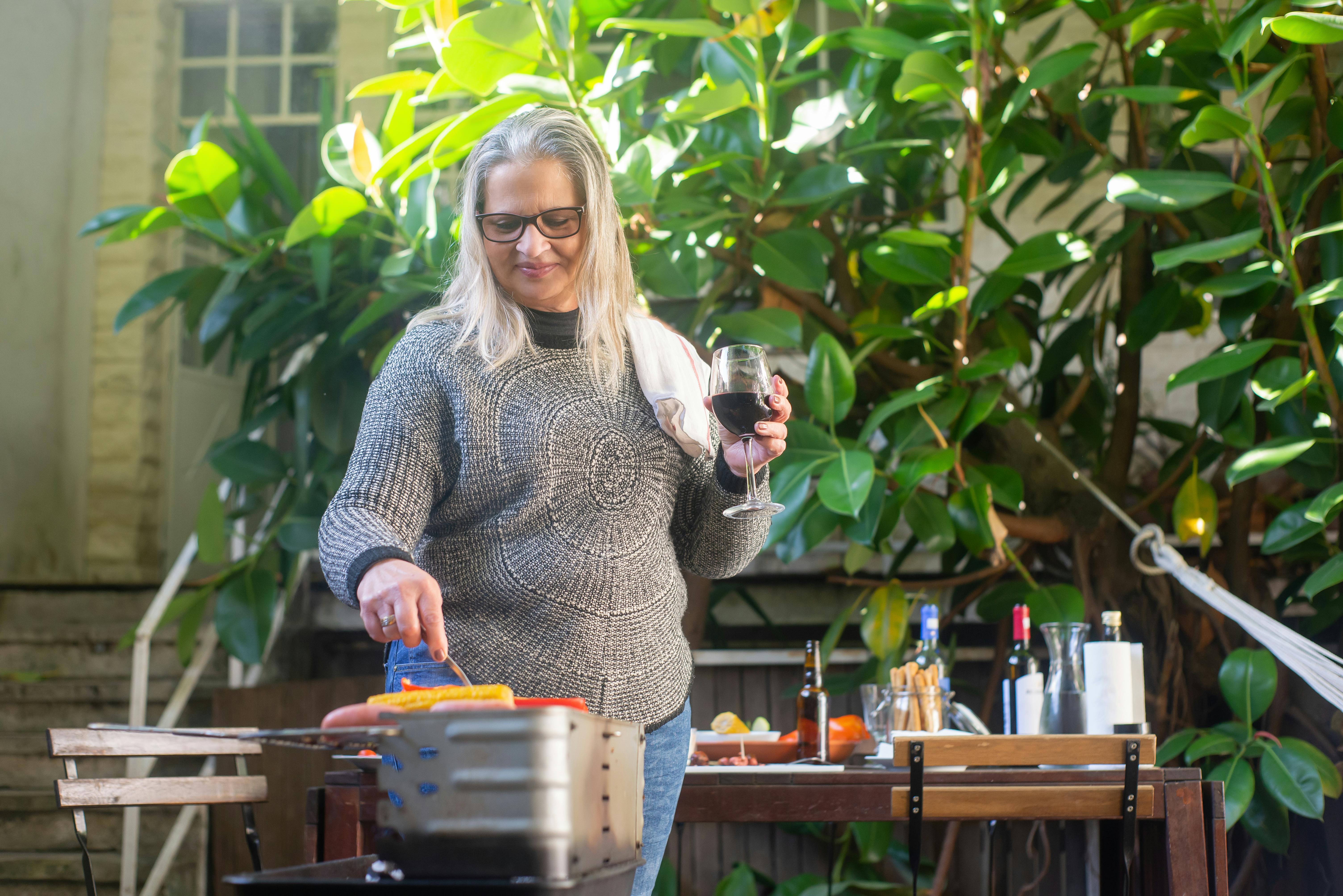 woman making a barbecue while holding a glass of wine