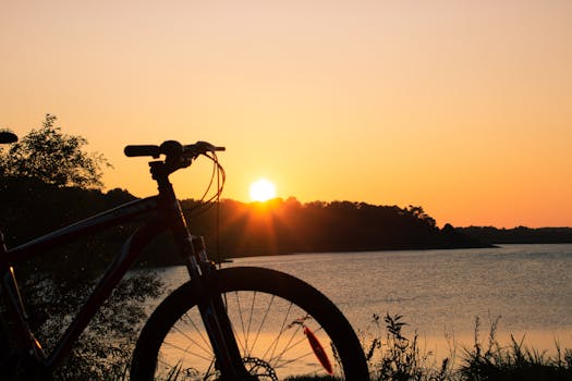 Silhouette of a bicycle with a stunning sunset over a tranquil lake, evoking adventure and calm.