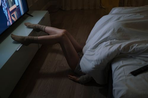 Free A person lounging on the floor by a bed watching television in a dimly lit bedroom. Stock Photo