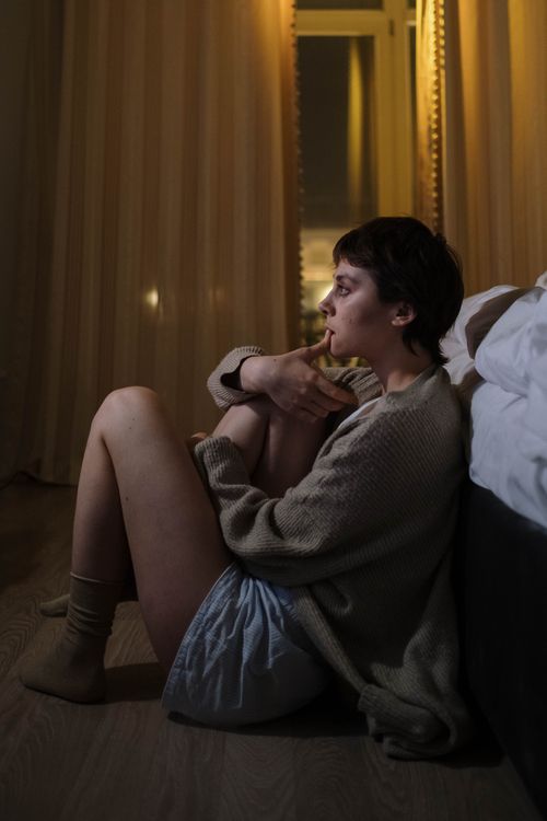 Free A woman sits on the floor beside her bed, deep in thought, illustrating themes of contemplation and mental health. Stock Photo