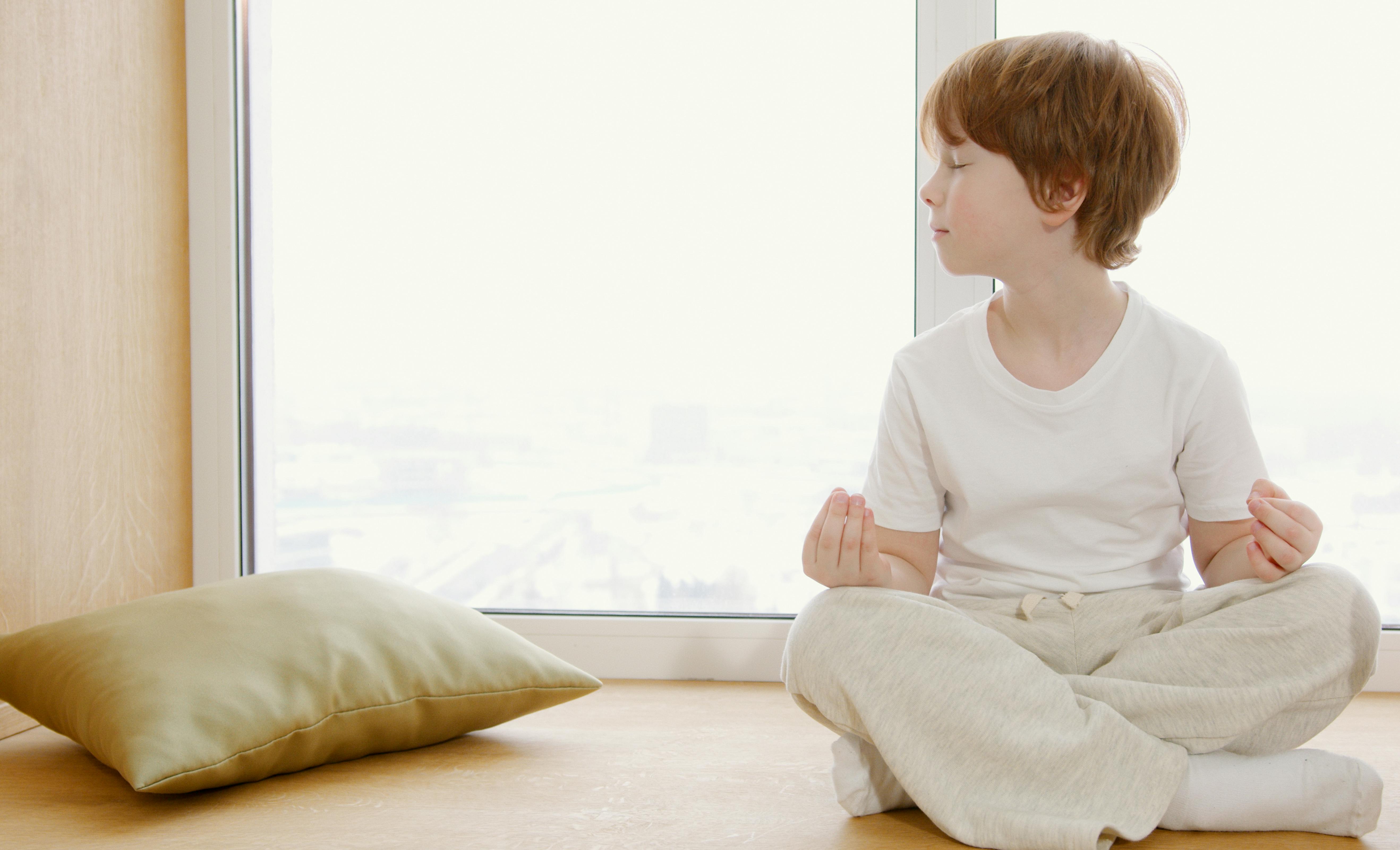 Free A young child practicing meditation indoors near a sunny window. Stock Photo