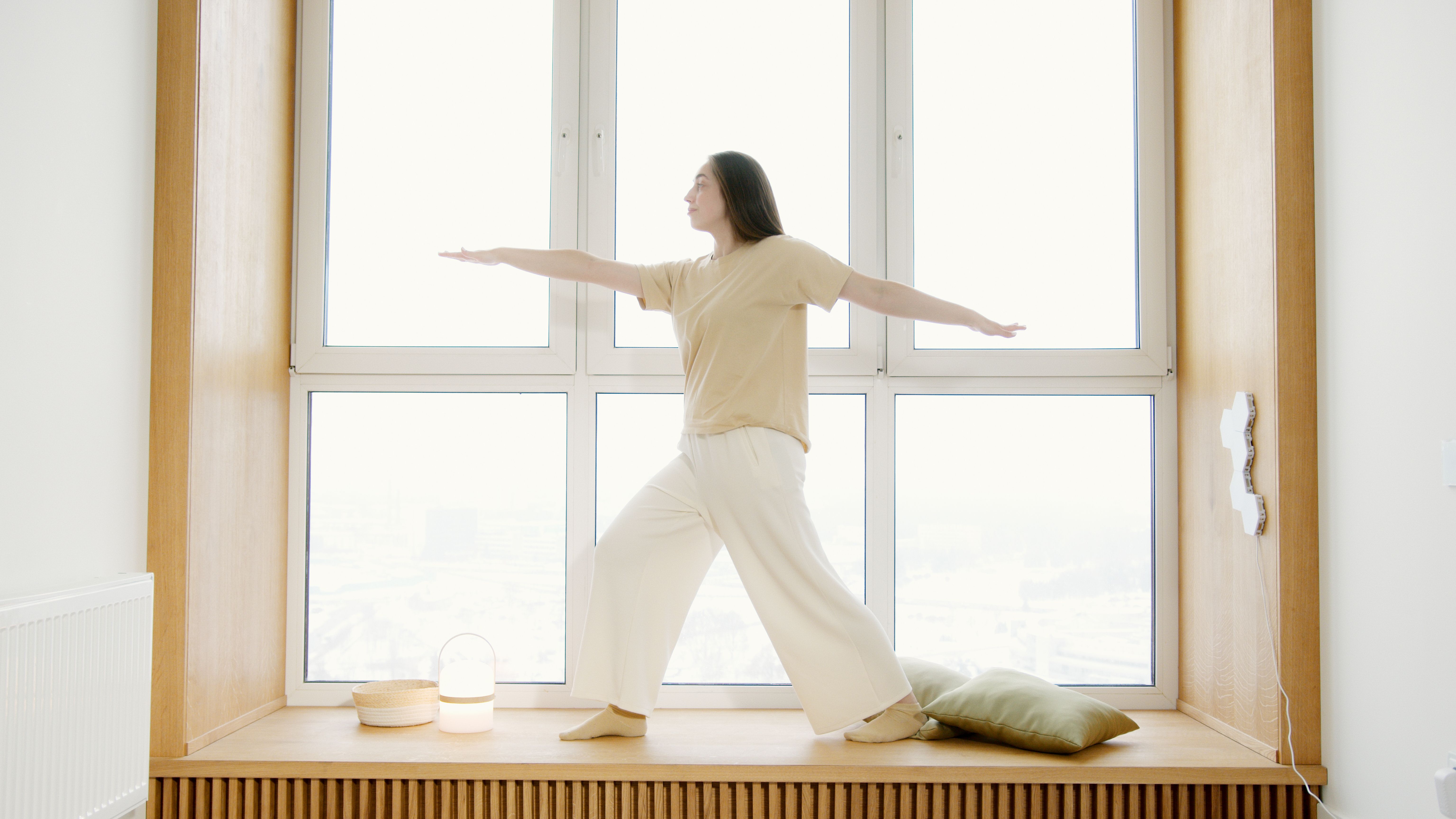 A woman balances in a yoga pose on a windowsill with natural light.