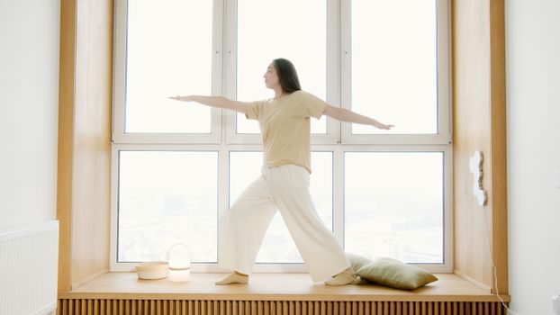 A woman balances in a yoga pose on a windowsill with natural light.
