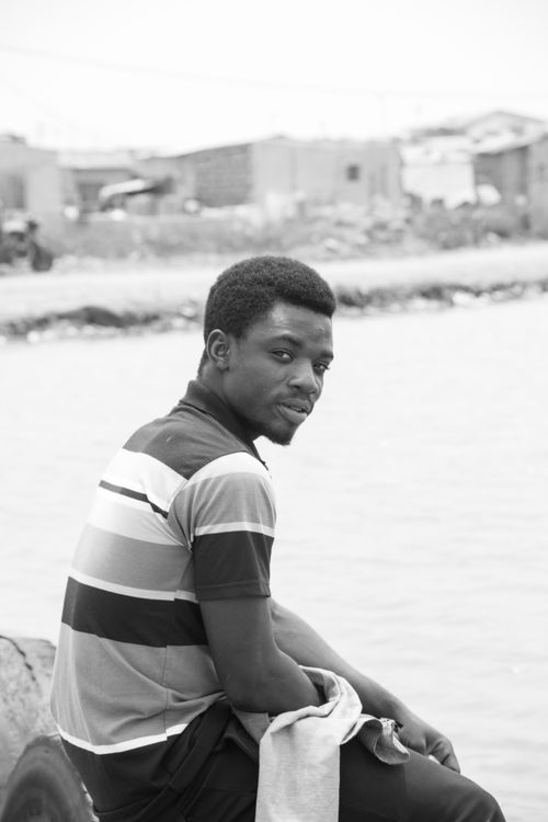 Free A contemplative man sitting by the water's edge in a black and white portrait. Stock Photo
