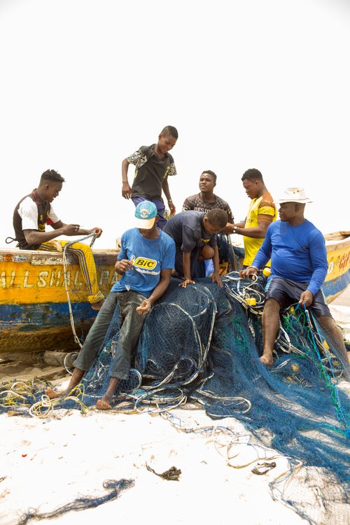 Free Men working together to mend fishing nets on a colorful boat, showcasing teamwork and traditional techniques. Stock Photo