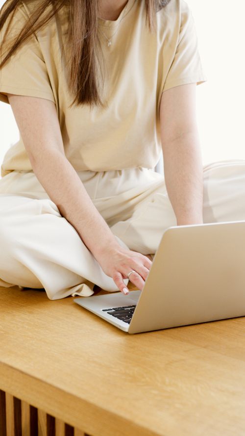 Free Young woman sitting cross-legged on a wooden bench working on a laptop indoors. Stock Photo