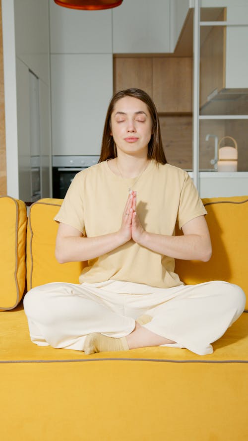 Free Woman Sitting on Yellow Sofa While Meditating Stock Photo