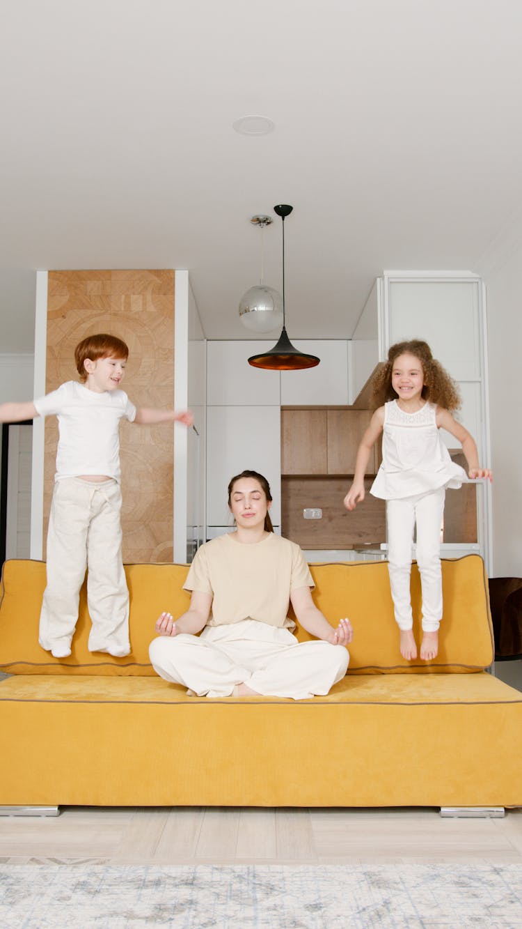 Children Jumping On Sofa Near A Woman 