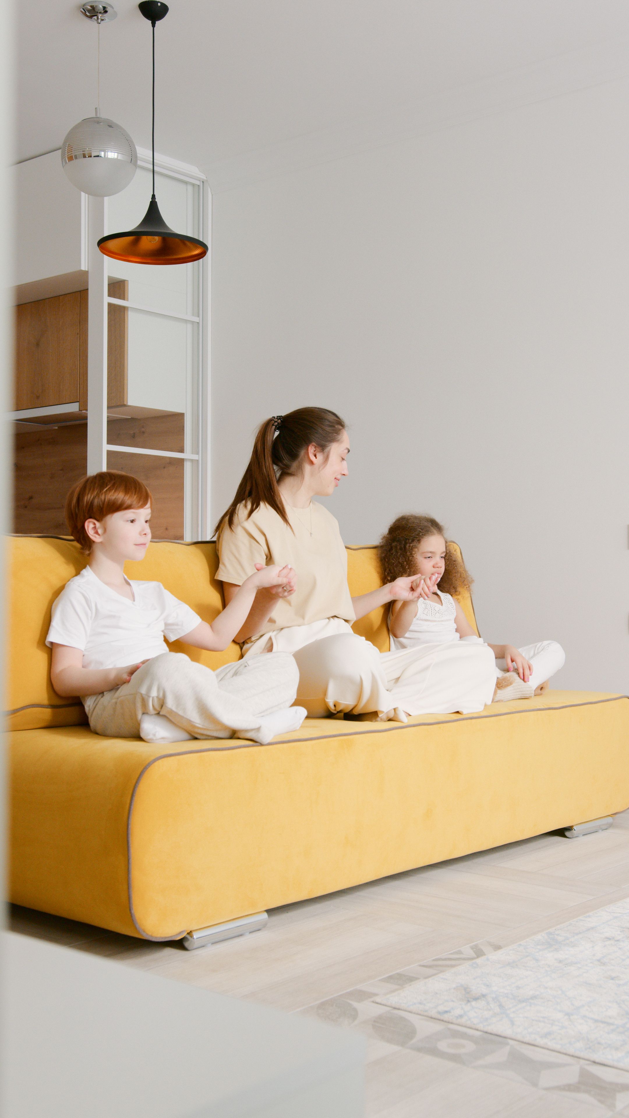Mother and children enjoy quality time together on a stylish yellow sofa in a bright living room.