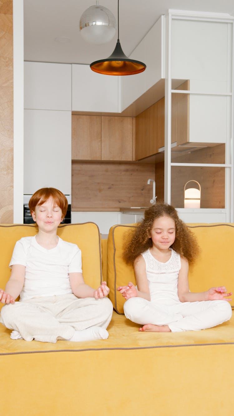 Two Children Meditating On A Yellow Sofa