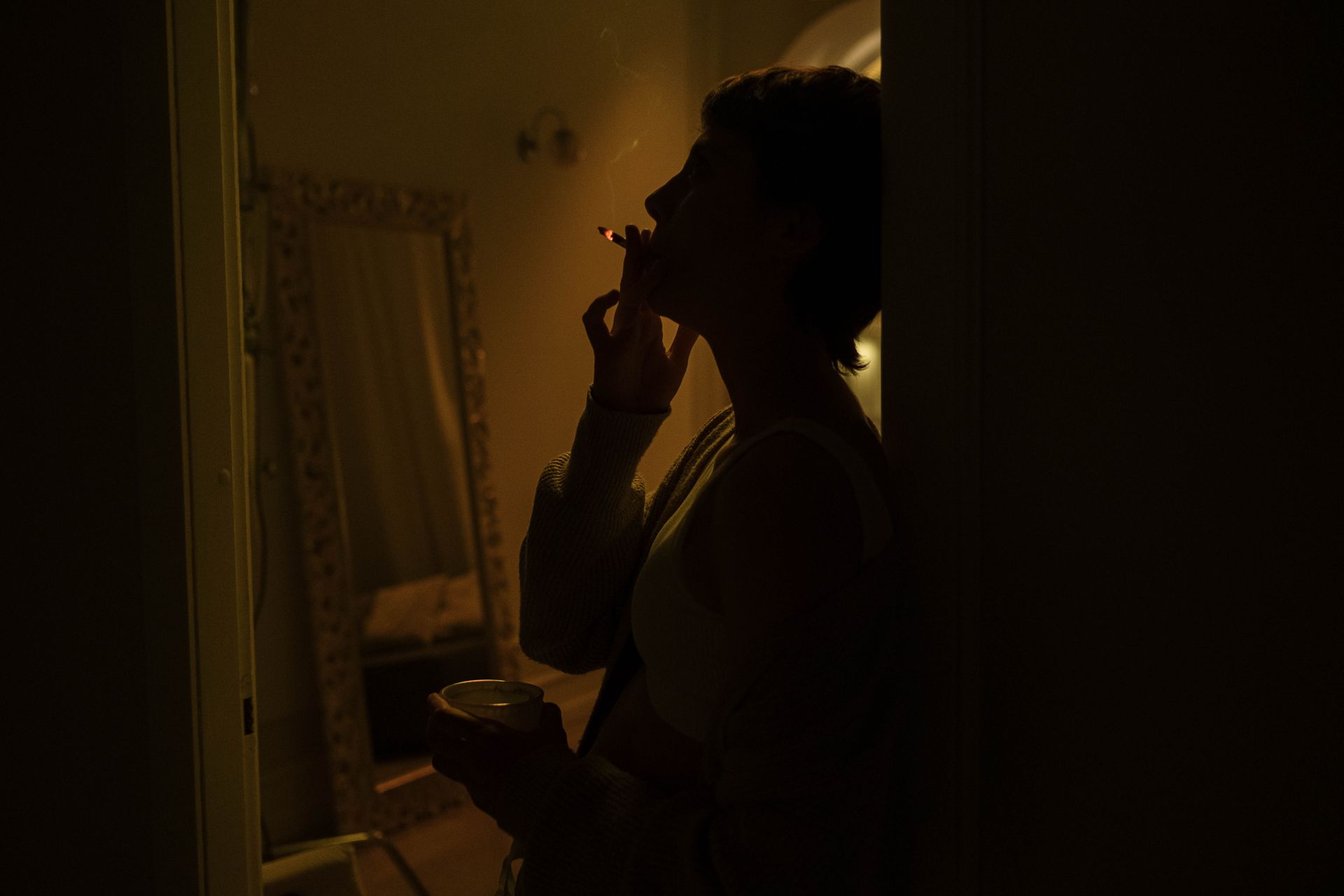 A moody silhouette of a woman smoking indoors, creating an atmospheric scene at night.