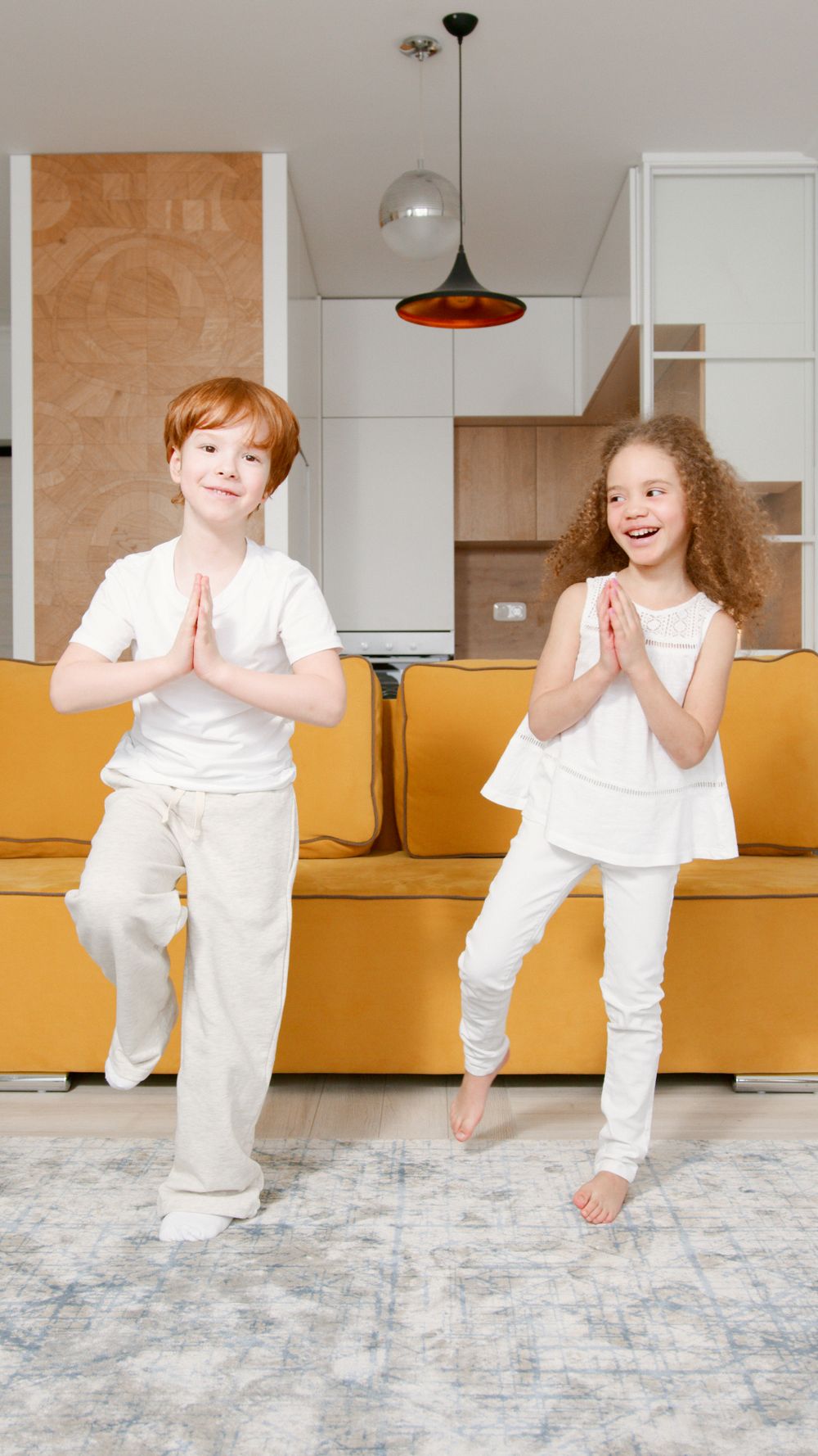 Two children practicing yoga tree pose at home