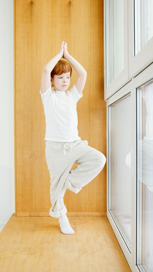 Free Young redheaded child performing yoga inside near window. Stock Photo