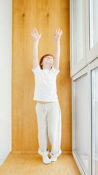 Young boy stretching with arms raised indoors, embodying a healthy lifestyle.