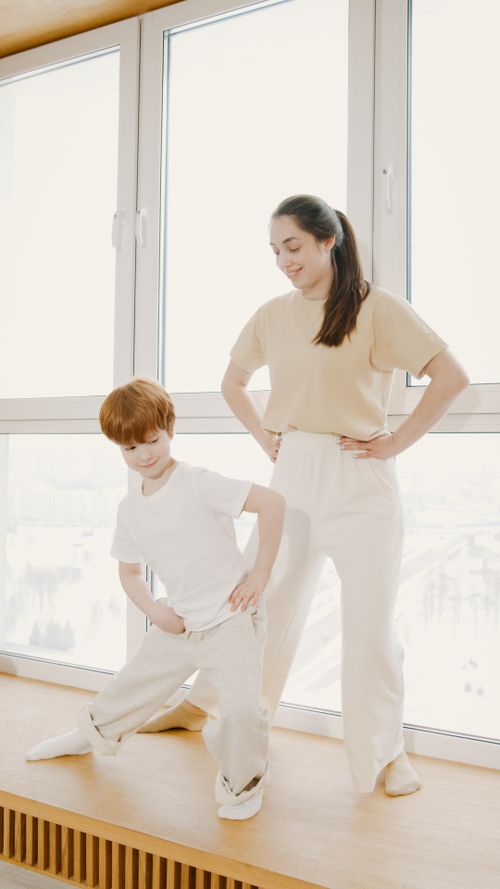 Free A woman and child practicing yoga poses indoors by a sunny window, promoting family fitness. Stock Photo