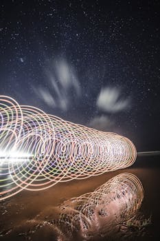 星光熠熠的夜空下，海滩上色彩缤纷的螺旋光轨迹反射着光芒，令人着迷