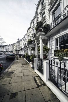 Cityscape of residential houses facades located along sidewalk of city road with columns at entrance and balconies decorated with green plants