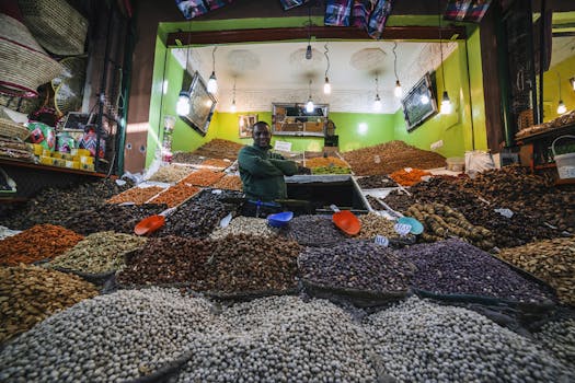 From below of African American man standing between market stalls with multi colored dried fruits and nuts illuminate with light bulbs