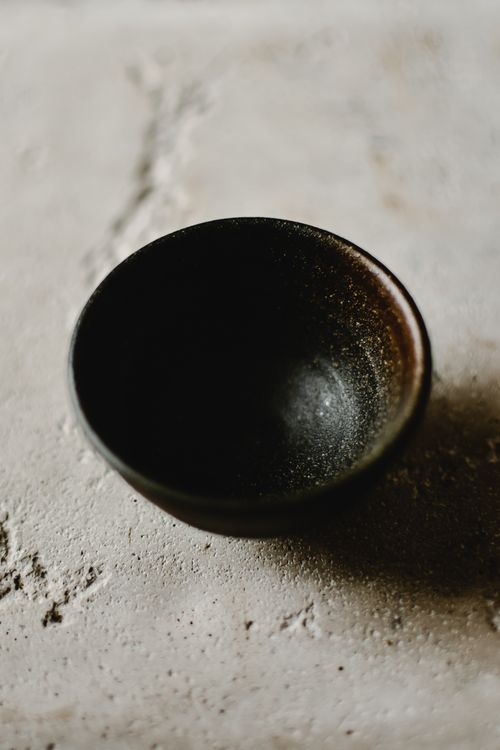 Free Artistic close-up of a rustic black ceramic bowl on a textured concrete surface. Stock Photo