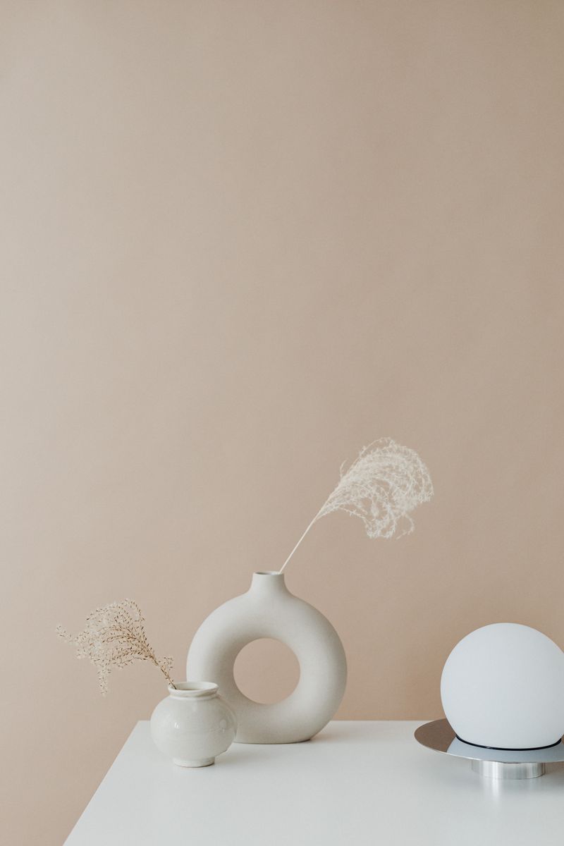 Elegant minimalist setup featuring a white vase with dry grass and a spherical lamp on a table.