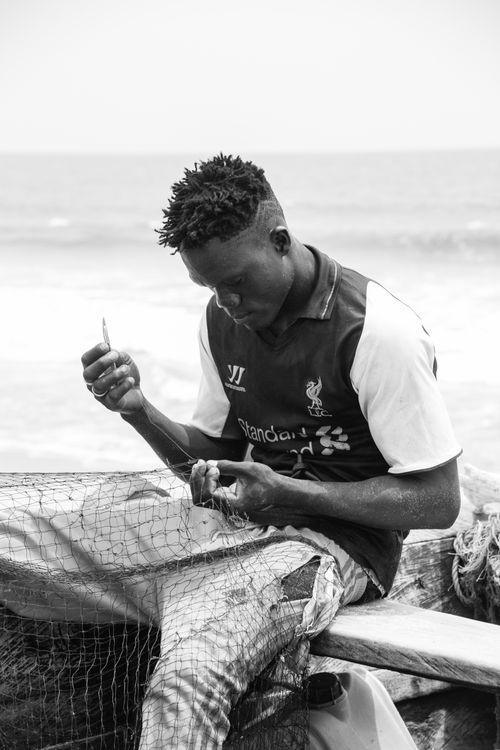 Free Black and white portrait of a man mending a fishing net by the sea. Stock Photo