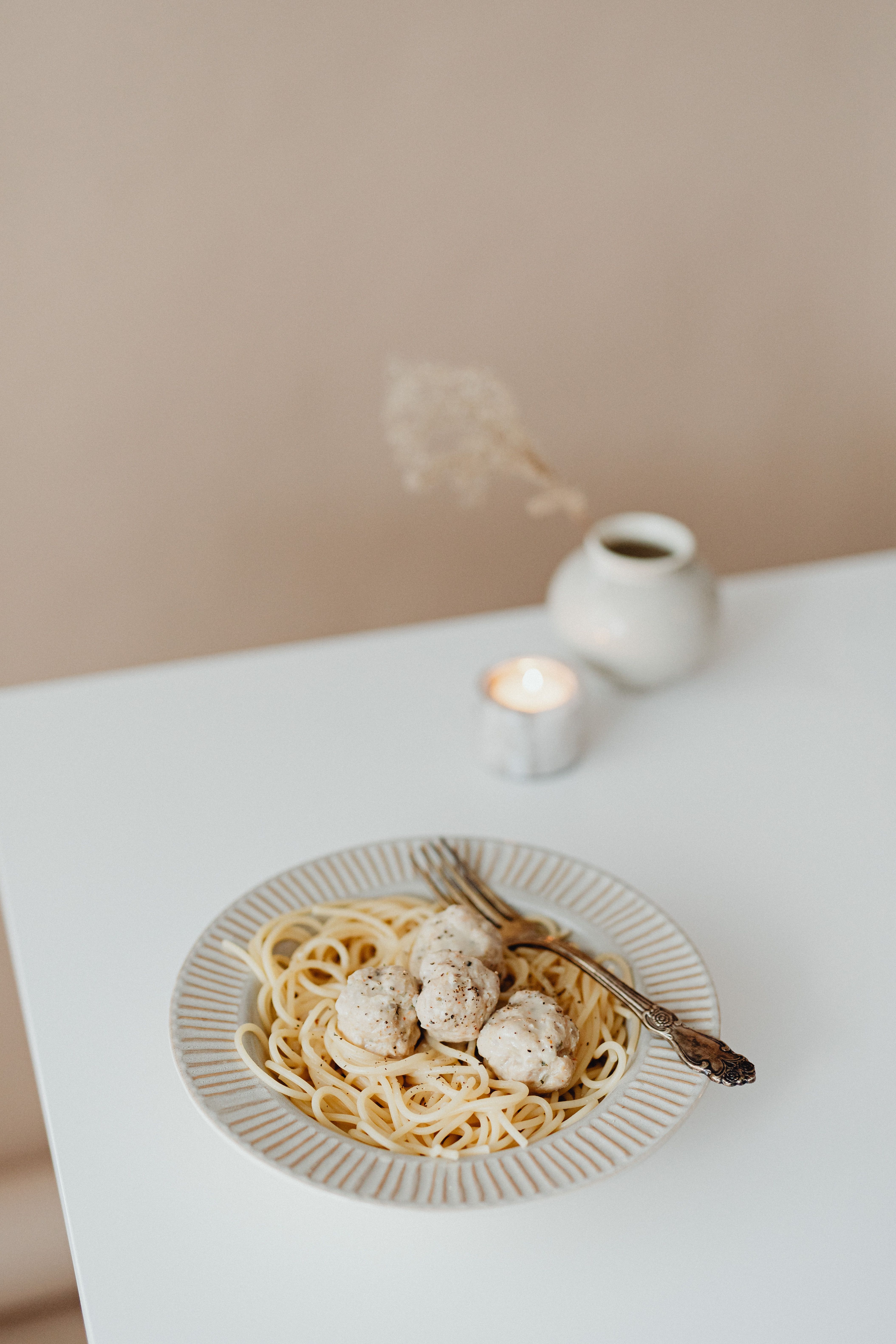 Plate of pasta with meatballs on a white table setting for a cozy indoor meal.